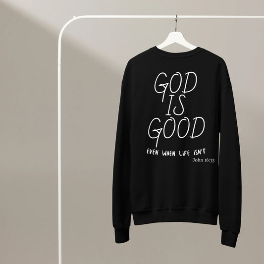 Black sweatshirt with 'God is Good even when life isn't' text on a hanger against a beige background